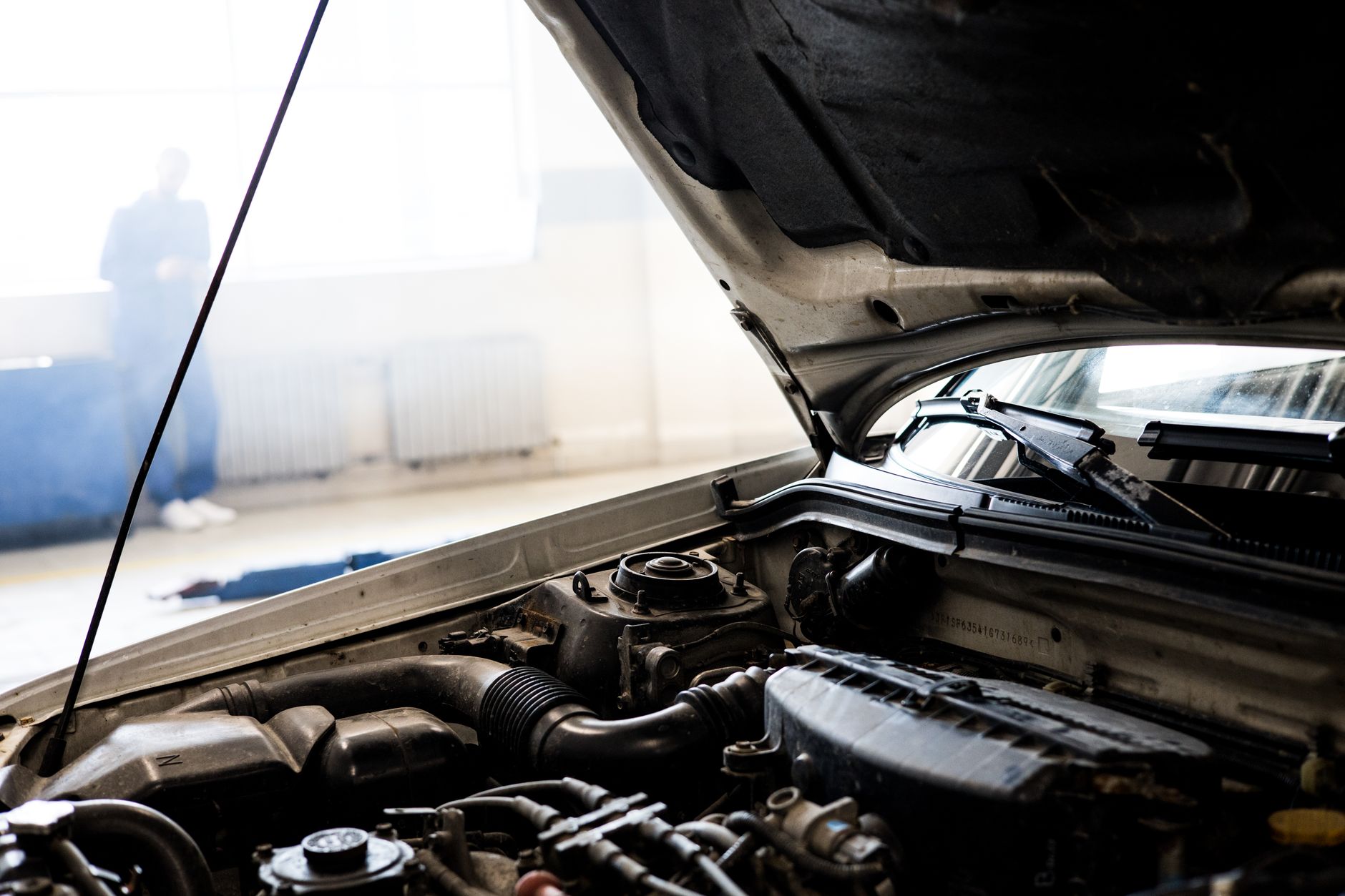 Car with its hood up in a repair shop, engine bay in the foreground