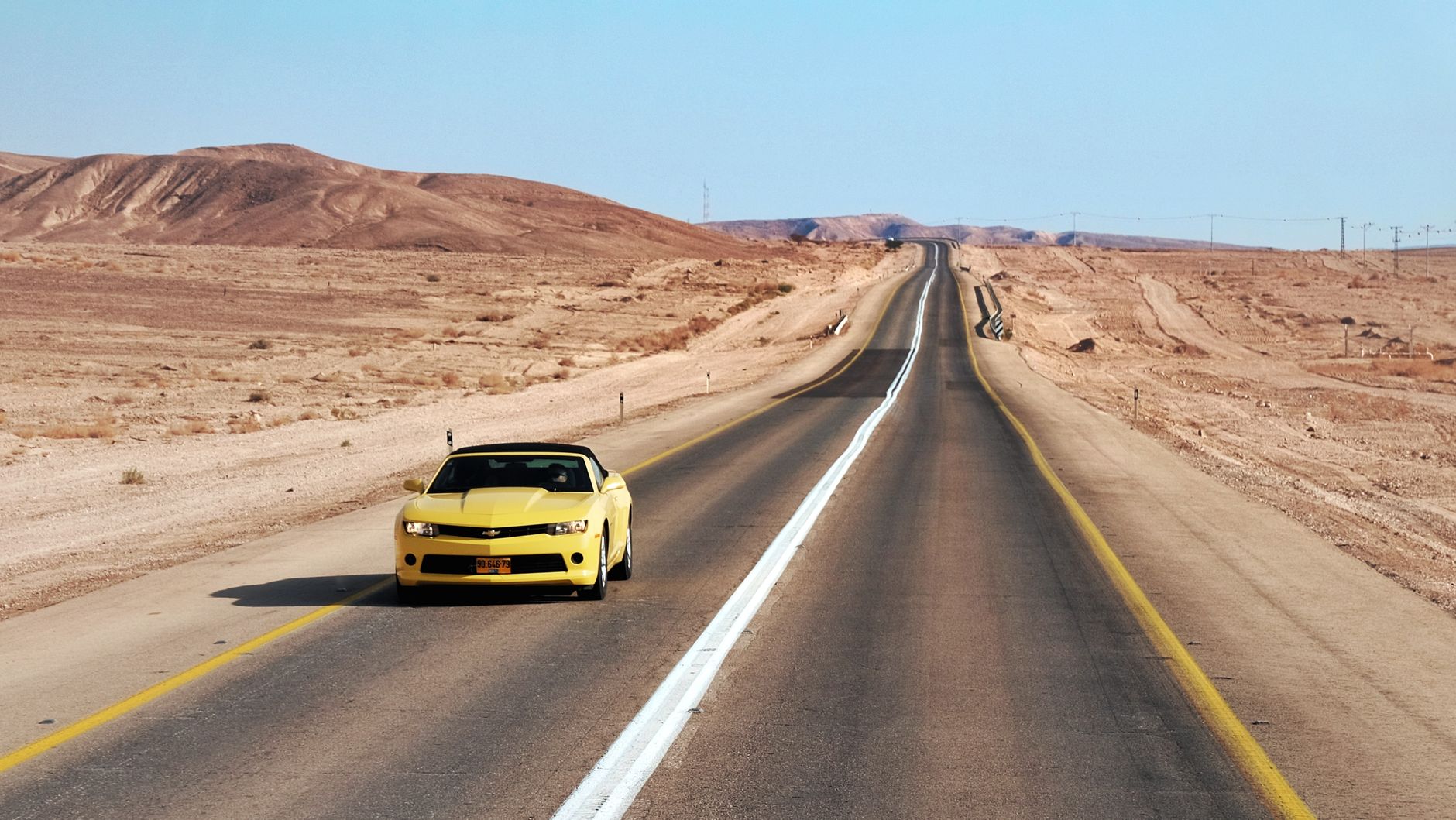Yellow car driving on an empty desert highway under a clear sky