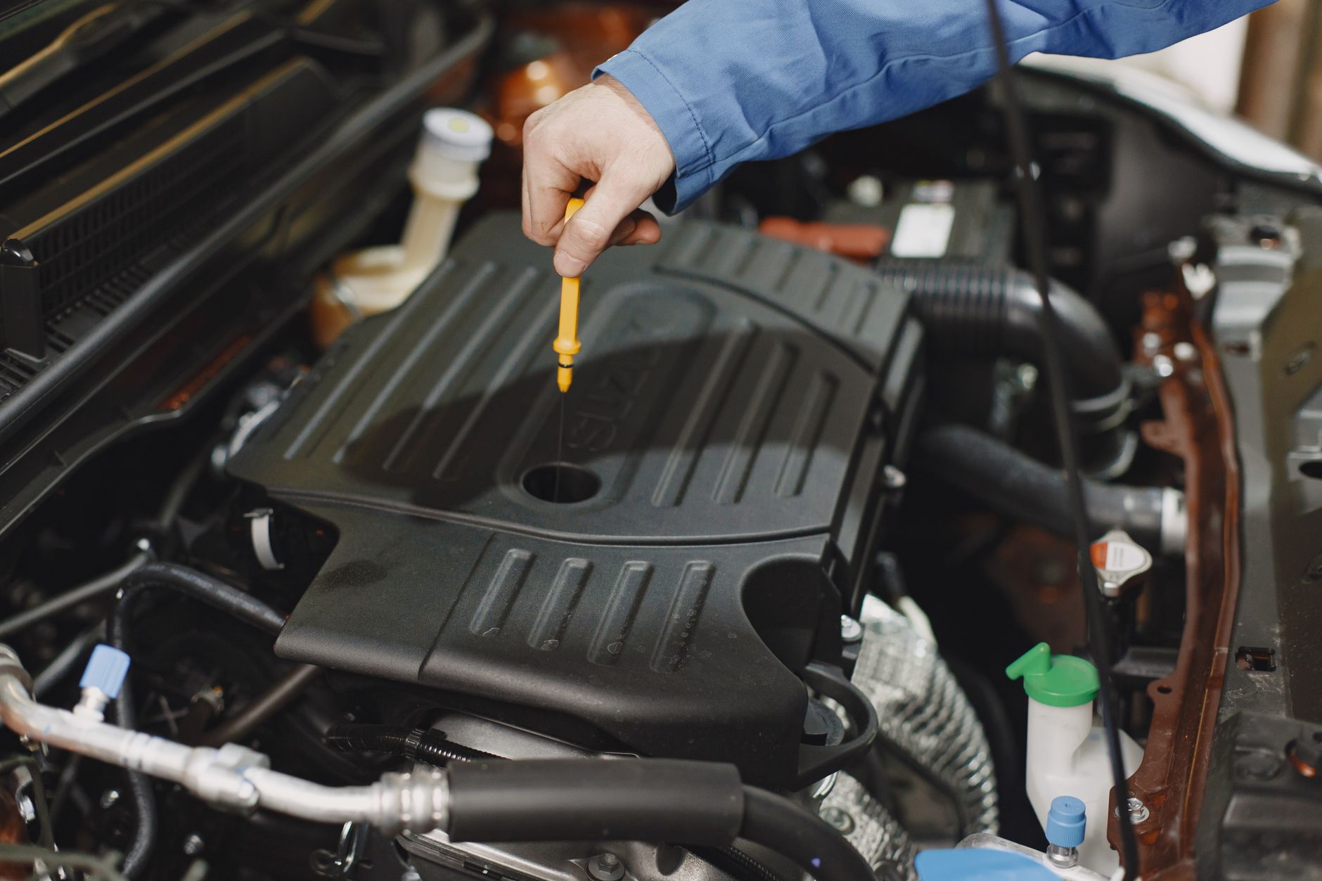 Technician checking fluid with a dipstick in a car's engine bay