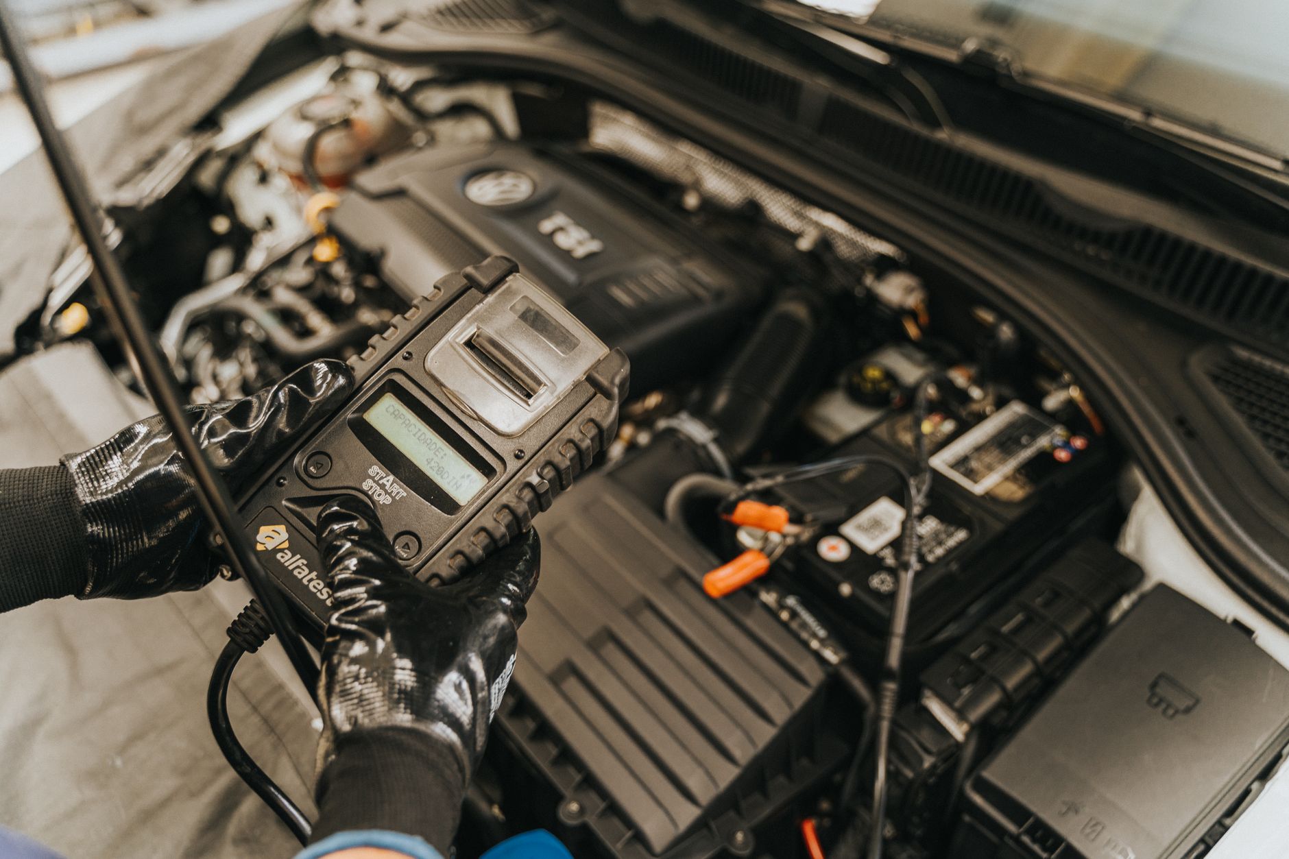 Gloved hands holding a diagnostic scanner over an open engine bay