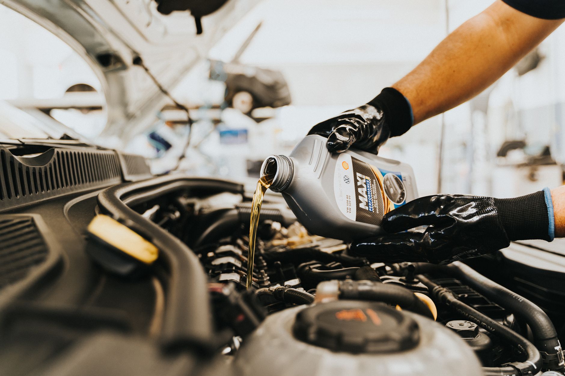 Gloved hands pouring fluid from a bottle into a car engine in a repair shop