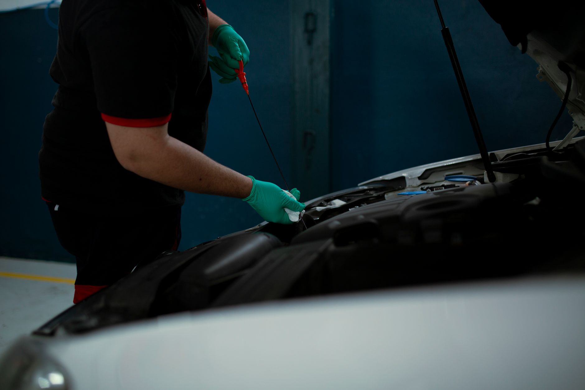Mechanic in gloves pulling a dipstick from under a car hood in a workshop