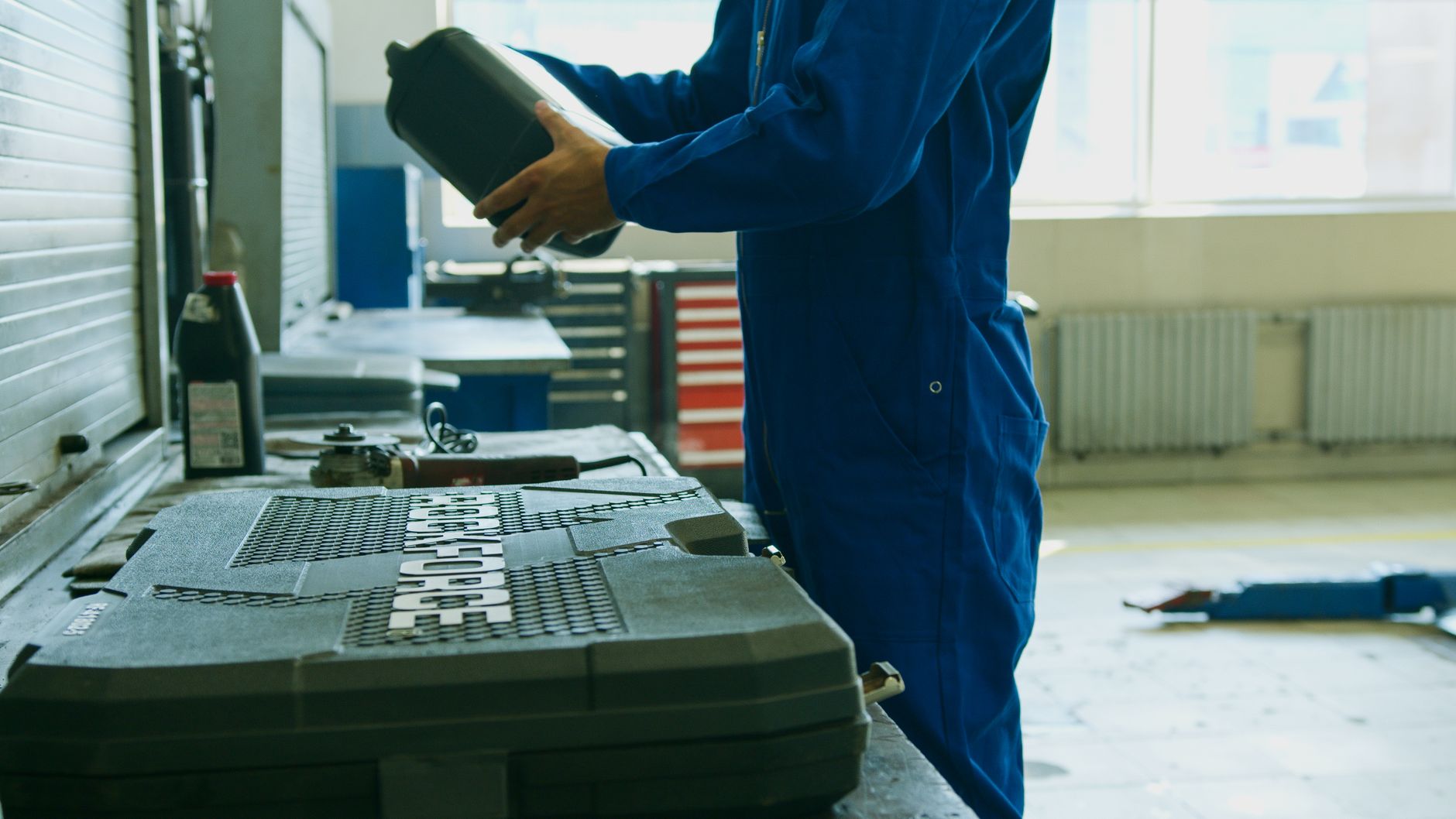 Mechanic in blue overalls holding a bottle of fluid at a workbench in a repair shop