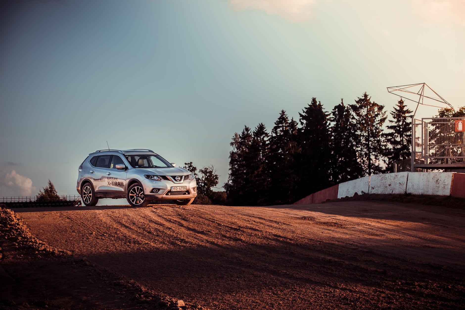 Silver Nissan crossover parked on a dirt road at sunset