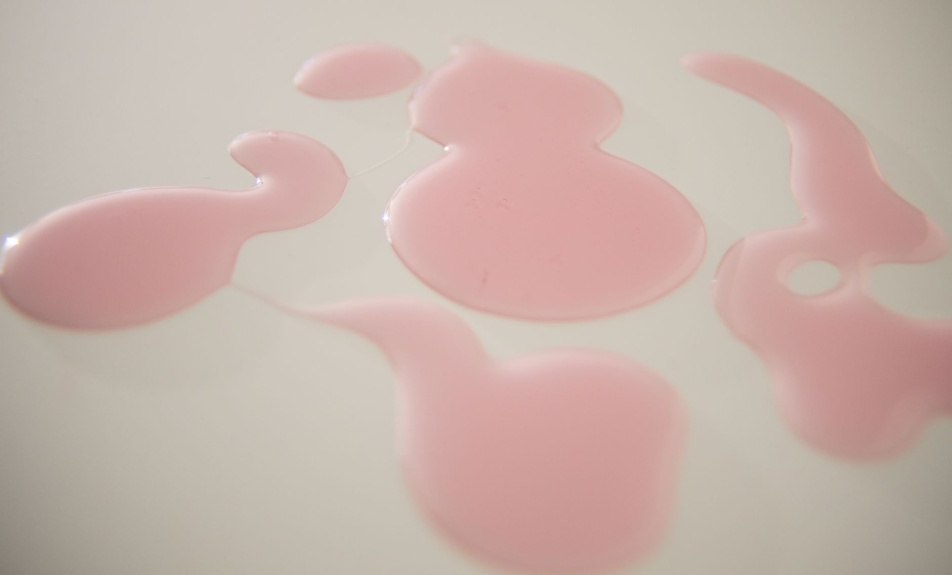 Drips of pale pink fluid on a white surface