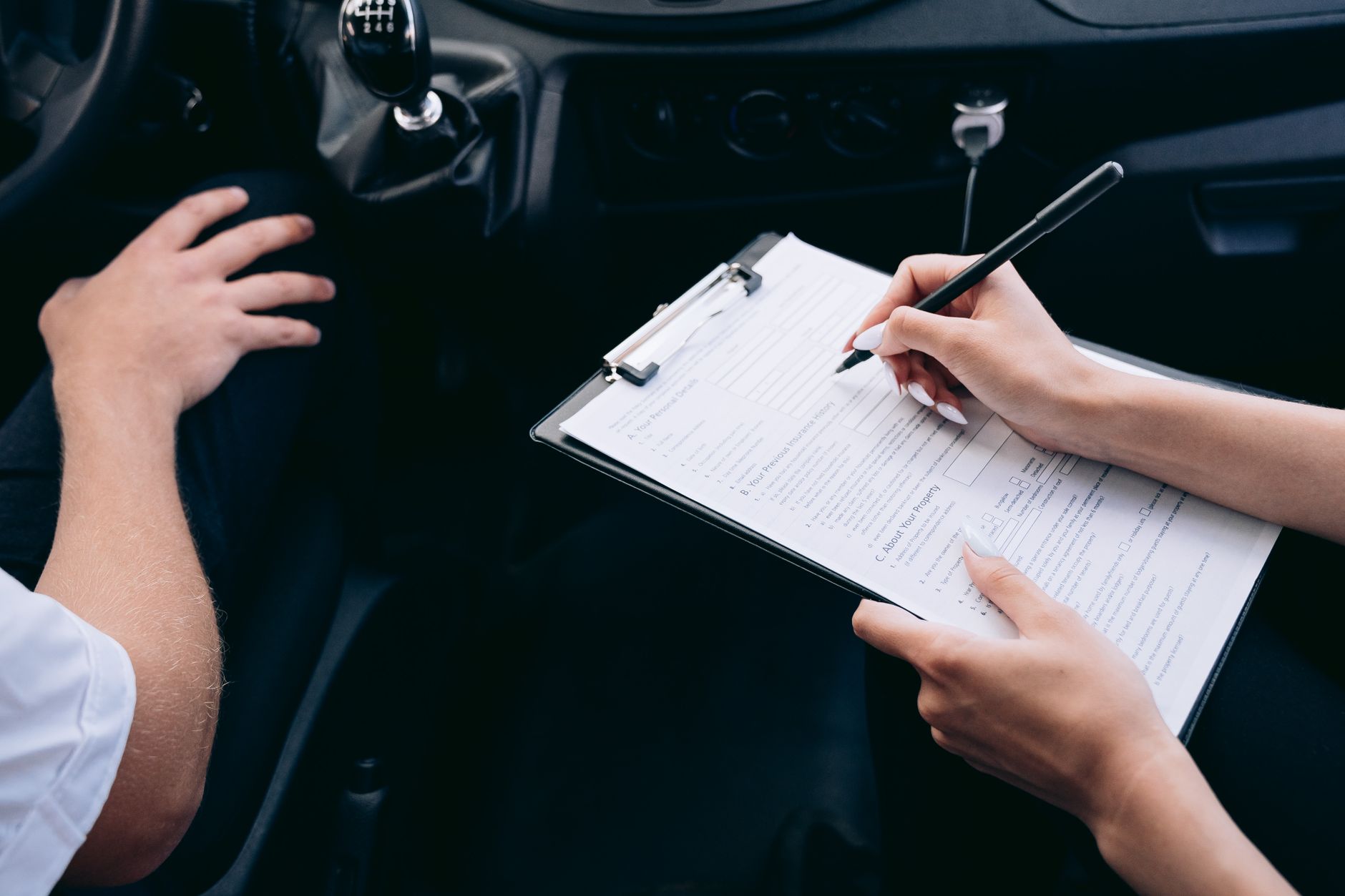Hands writing a repair estimate on a clipboard inside a car